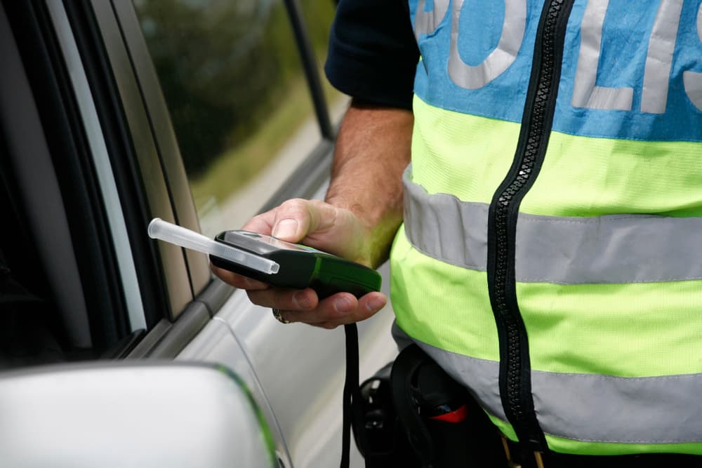 Policeman holding device for checking alcohol intoxication while standing near the stopped car