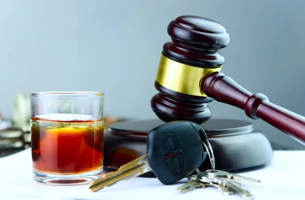 A judge's gavel sits beside a whiskey glass and car key, symbolizing the consequences of driving under the influence. 
