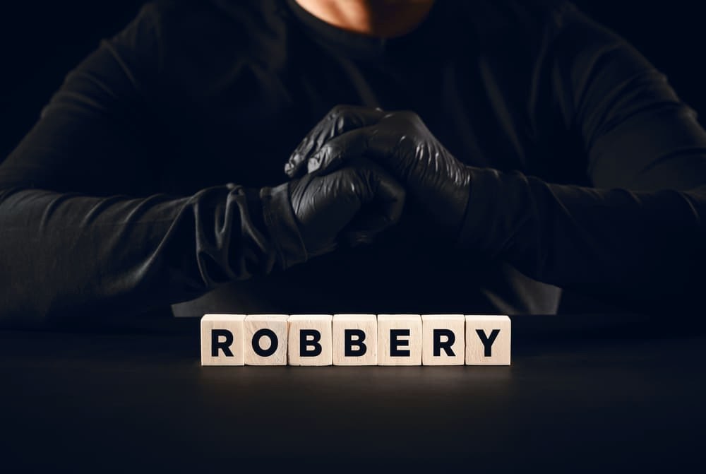 The word robbery written on wooden blocks with a thief with black gloves background