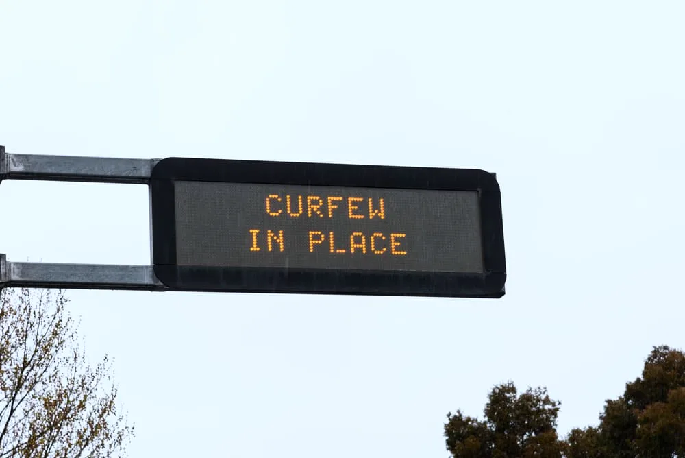 An overhead street sign showing the information about the curfew in place in the city